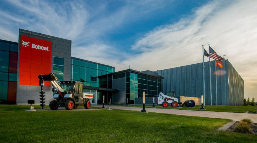 Exterior view of Bobcat building at unset with lush green grass and bobcat equipment displayed on lawn.