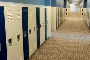 Hallway of lockers alternating in beige and black lockers with blue walls overhead and beige and brown carpet underneath.