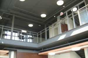 Upper mezzanine with metal and cable railings with small tables and chair throughout as seen from lower level.