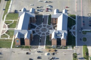 Aerial view of NDSU Living Learning Center buildings with red brick and gray metal roofing surrounded by lush green and flower courtyards to the buildings' fronts.
