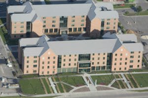 Aerial view of NDSU Living Learning Center buildings with red brick and gray metal roofing surrounded by lush green and flower courtyards to the buildings' fronts.