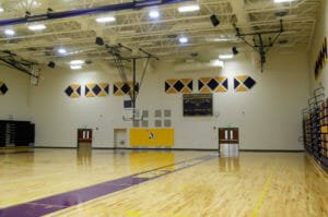 High school gymnasium with bright wooden planked flooring with purple and gold accents throughout.