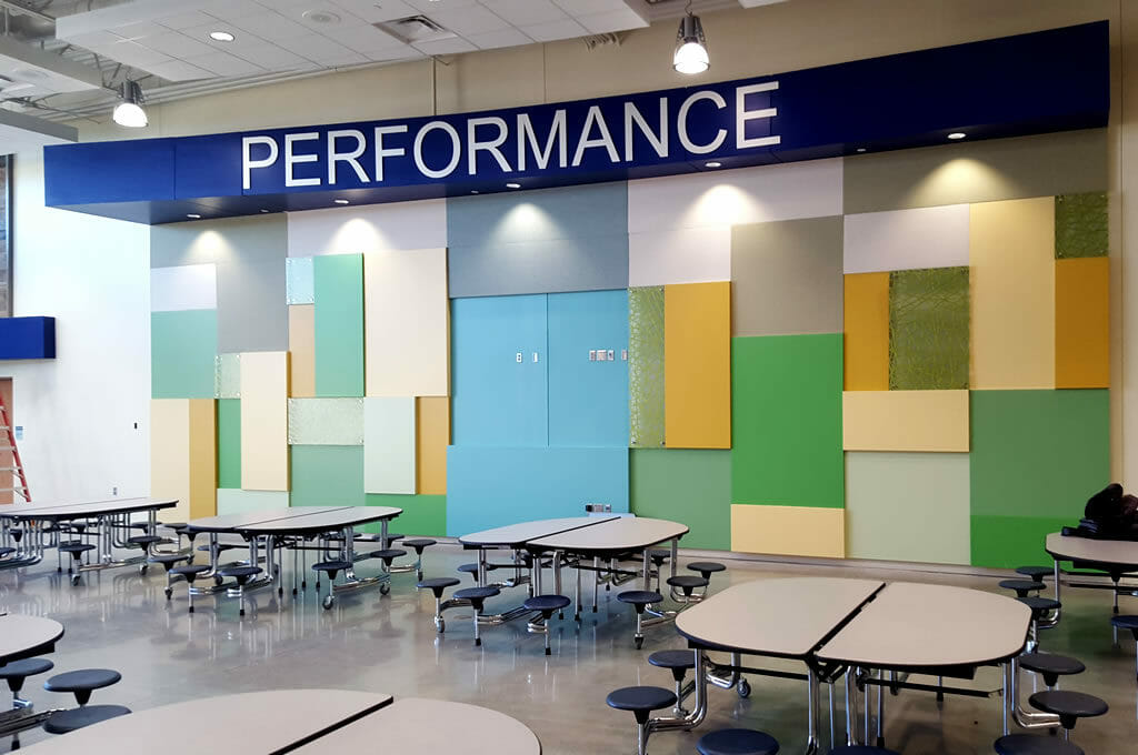 Interior two-story tall accent wall with the word "PERFORMANCE" at the top with panels of light blue, green, yellow, and gray underneath.