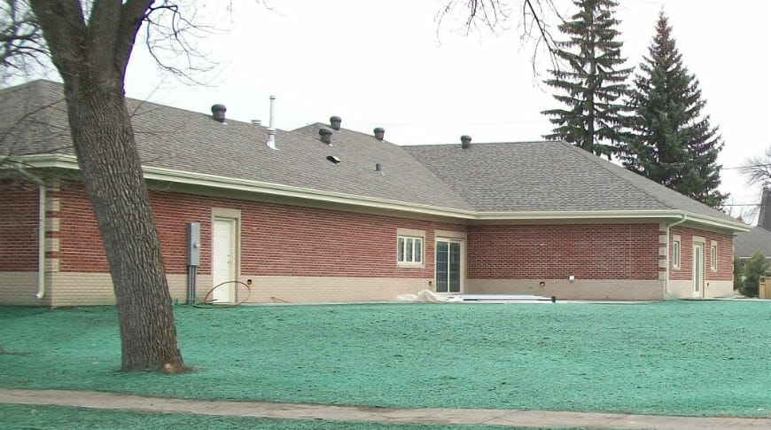 Exterior of one-story red brick building with dark gray shingles and bright green grass seed in front.