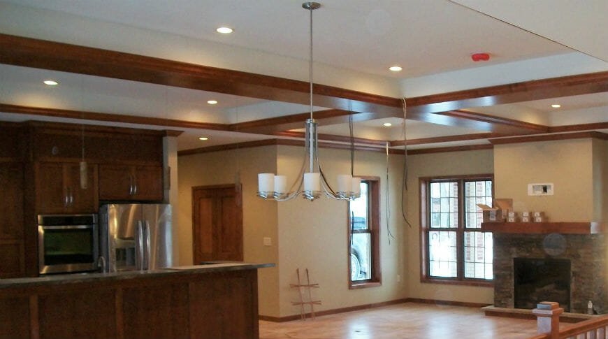 Interior view of St. John's rectory showing cherry-wood kitchen cabinetry and stainless steel appliances to the left and stone fireplace with wooden mantel to the right.