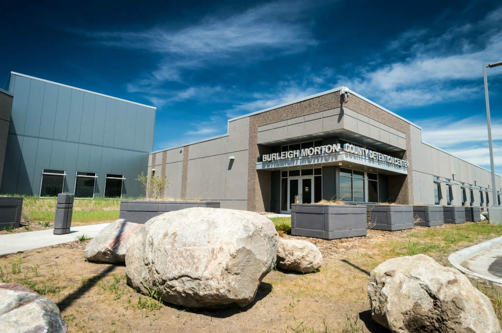 Exterior of Burleigh Morton County Detention Center with gray concrete planter boxes around the side of the building and landscaping large boulders in front.