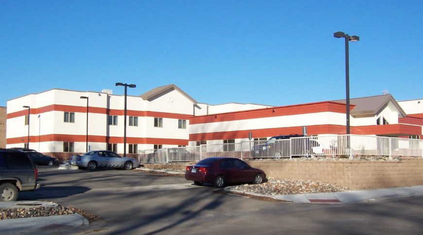 Beige and red striped two-story building with windows throughout and parking lot to the rear.