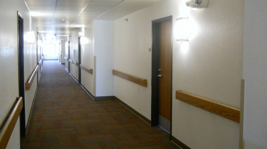 Interior hallway with wooden wall rails, brown and blue carpet squares and metal and wood doors on each side.