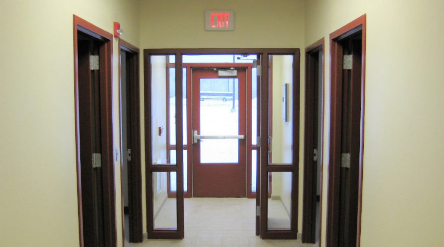 Side entrance with dark maroon metal doors and beige walls with Exit sign overhead.