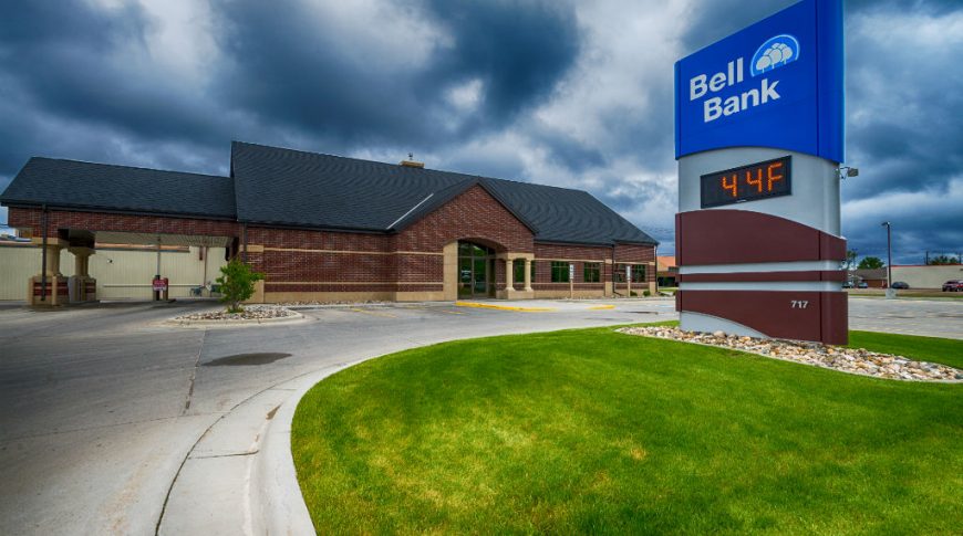 Exterior view of dark red bricked building with digital sign in foreground with "Bell Bank" logo on blue background.