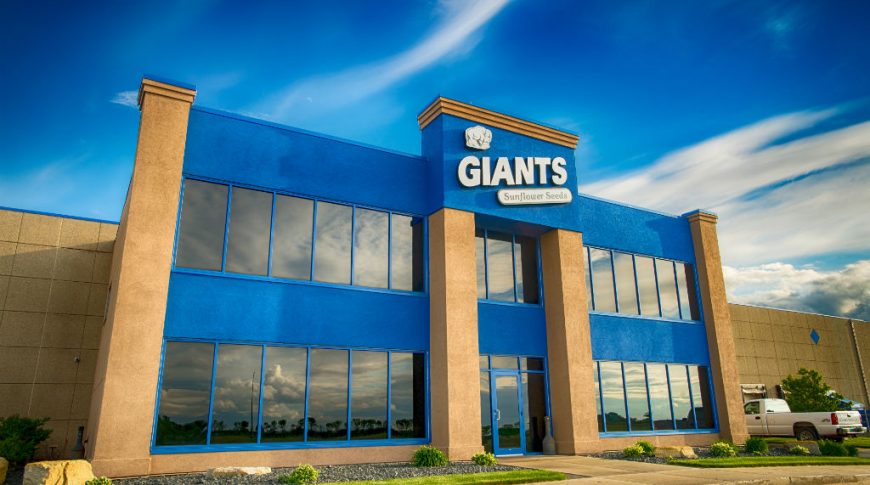 Close-up view from parking lot of GIants Sunflower Seeds 2-story beige and blue building entrance.