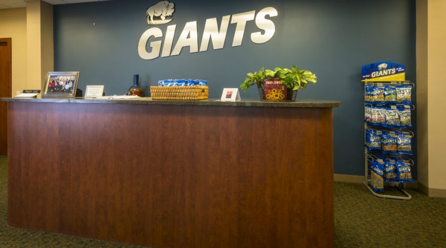 Interior reception area with tall cherry-wood desk and granite countertops with dark blue accent wall behind with the metal "Giants" logo.