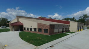 Aerial view of light concrete precast building with red brick and red entrance awning.