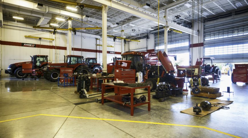 Large equipment shop with concrete floors and red workstations and toolboxes at each station. Red Case IH tractors at each station.