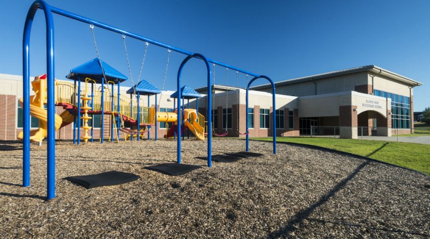 Primary-colored playground with red-bricked school entrance to the background.