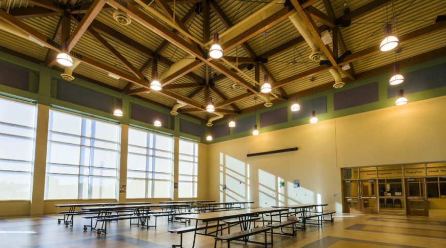 High-ceiling with wooden trusses with large tall windows to the back wall and folding cafeteria tables in the center.