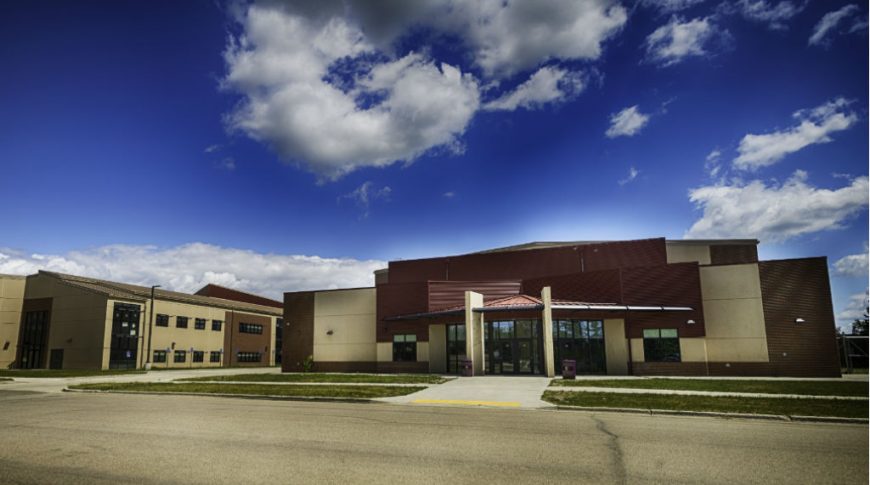 Street view of the front of a high school building with paved road in front and bright blue and white cloud background.