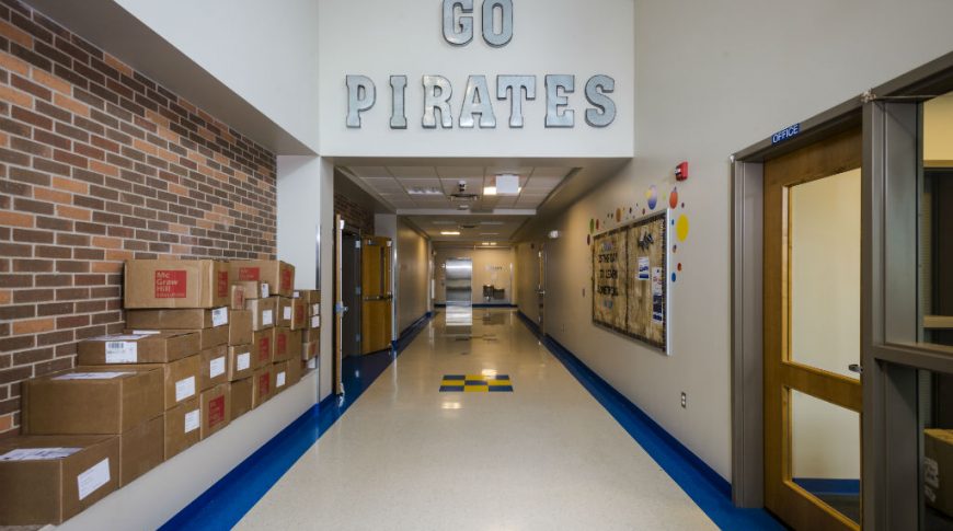 Long hallway with beige walls and metal letters saying "Go Pirates" overhead with brick wall to the left side.