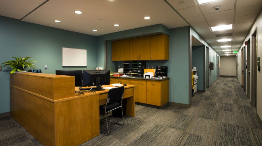 Administrative desk with maple cabinetry and teal walls behind with hallway to the right side