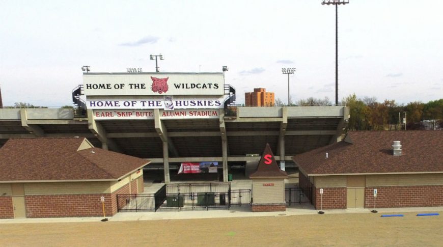 Back side of concrete stadium with brick buildings and parking lot beneath