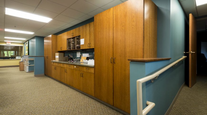 Wooden cabinetry with blue accent walls on either side, brown carpet below and fluorescent lights on paneled ceiling above