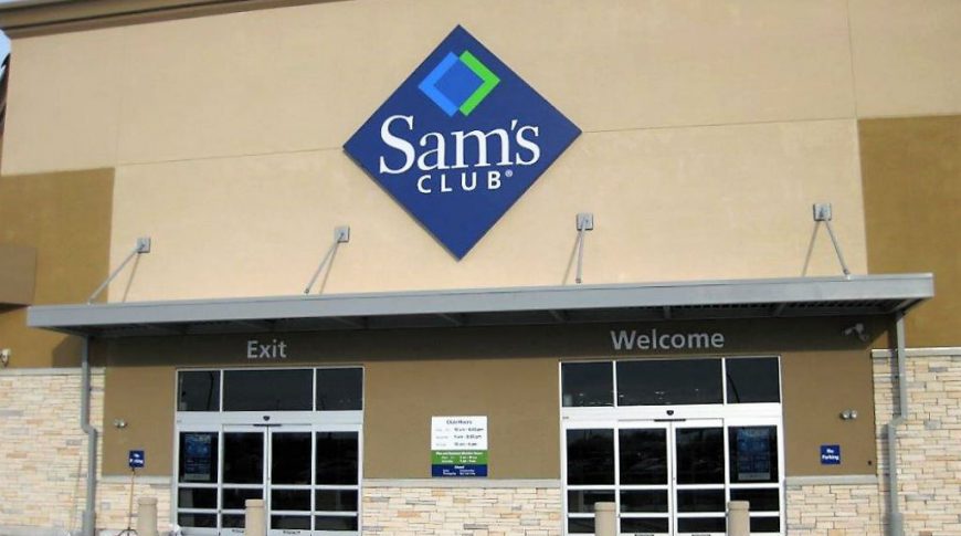 Close up entrance to beige building with automatic welcome and exit doors with the "Sam's Club" logo above.