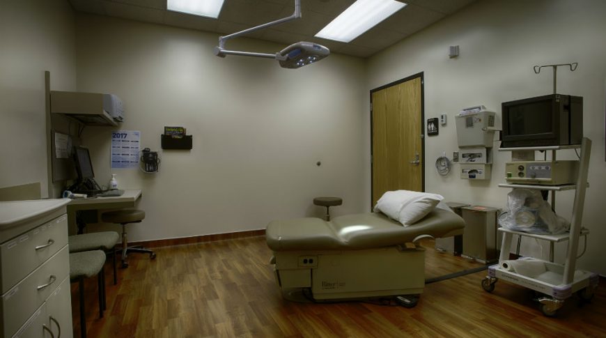 Exam room with beige walls and cabinetry, faux wood floors and medical equipment throughout