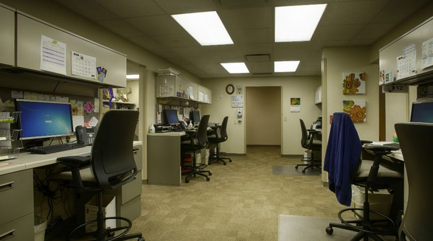 Beige room with beige walls, carpeting and ceiling with nurses desk stations on either side.