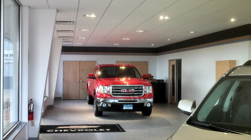 Vehicle dealership interior with large tiled floors, beige walls and ceiling tiles with a bright red truck showcased