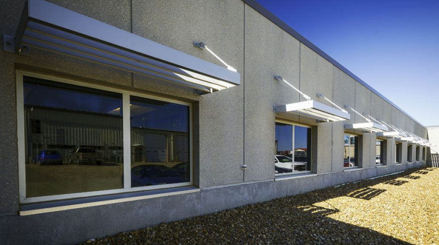 Exterior beige stucco wall with row of windows and metal awning above each