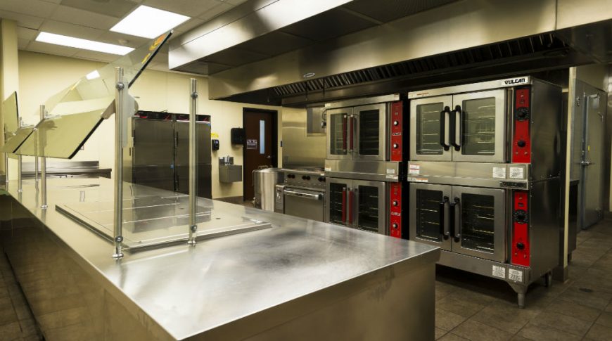 Stainless steel and red accented industrial kitchen appliances with stainless steel worktop to the center of the room