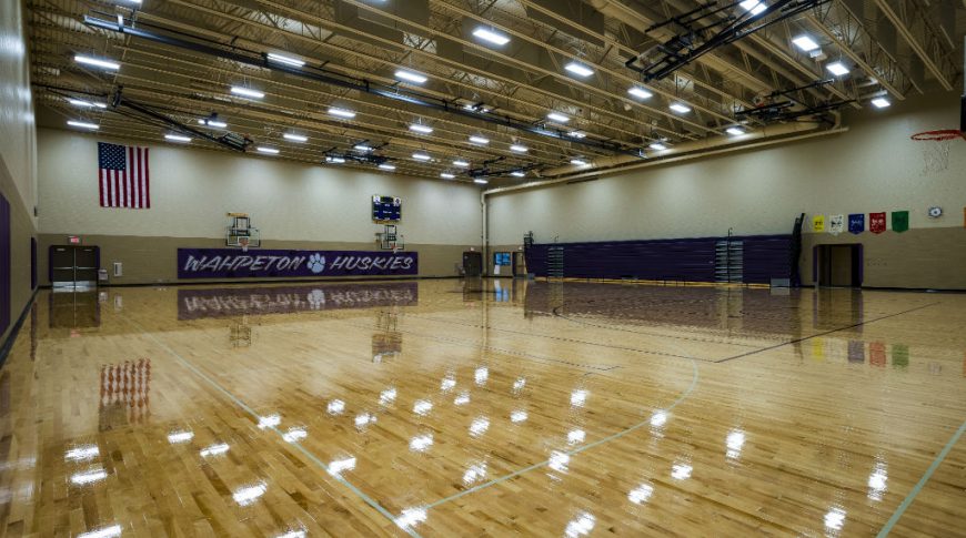 High School gymnasium with shiny newly buffed wooden floors, dark purple bleachers to the back right and Wahpeton Huskies sign to far back.