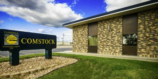 Comstock Construction's Wahpeton building with shades of brown brick and brown paneling with Comstock sign in foreground and bright blue sky in background.