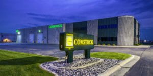 Fargo, ND's Comstock Construction precast concrete building with lit-up Comstock sign in the foreground at the entrance to the parking lot with blue dusk sky in background.
