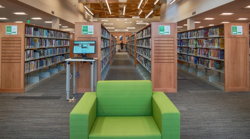 Bright green chair followed by rows of bookshelves behind and a beautiful wood trussed ceiling above.