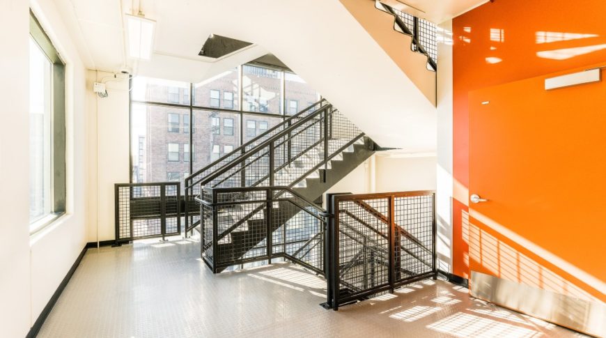 Interior stairwell in parking ramp with brightly colored orange accent wall, black staircase, and light beige walls and floor.