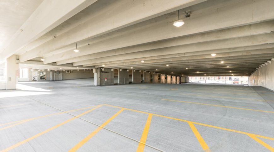 Interior of parking ramp showcasing concrete construction, yellow directional traffic arrows painted on the ground and parking spaces throughout.
