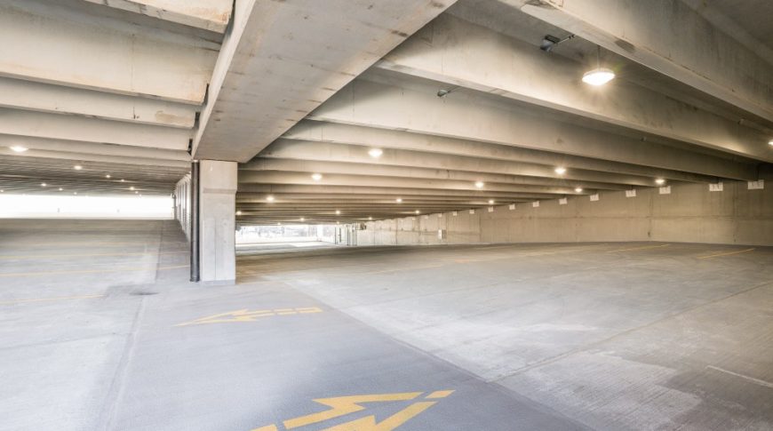 Interior of parking ramp showcasing concrete construction, yellow directional traffic arrows painted on the ground and parking spaces throughout.