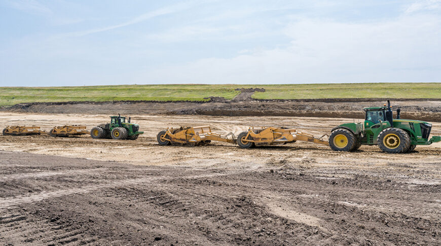 Two green tractors pulling earthwork machines in dirt field