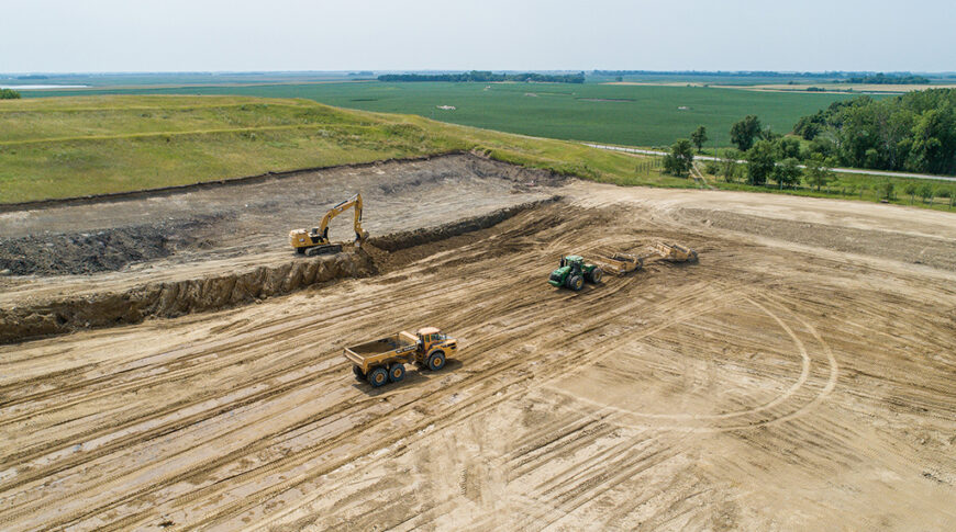Aerial view of dirt field with excavator, dump truck, and tractor implements
