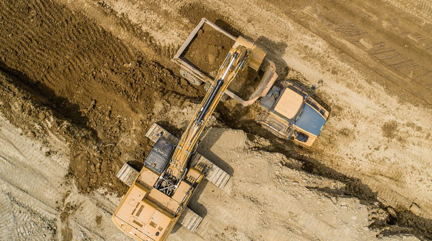 Aerial view straight overhead of excavator loading dirt into dump truck in dirt field