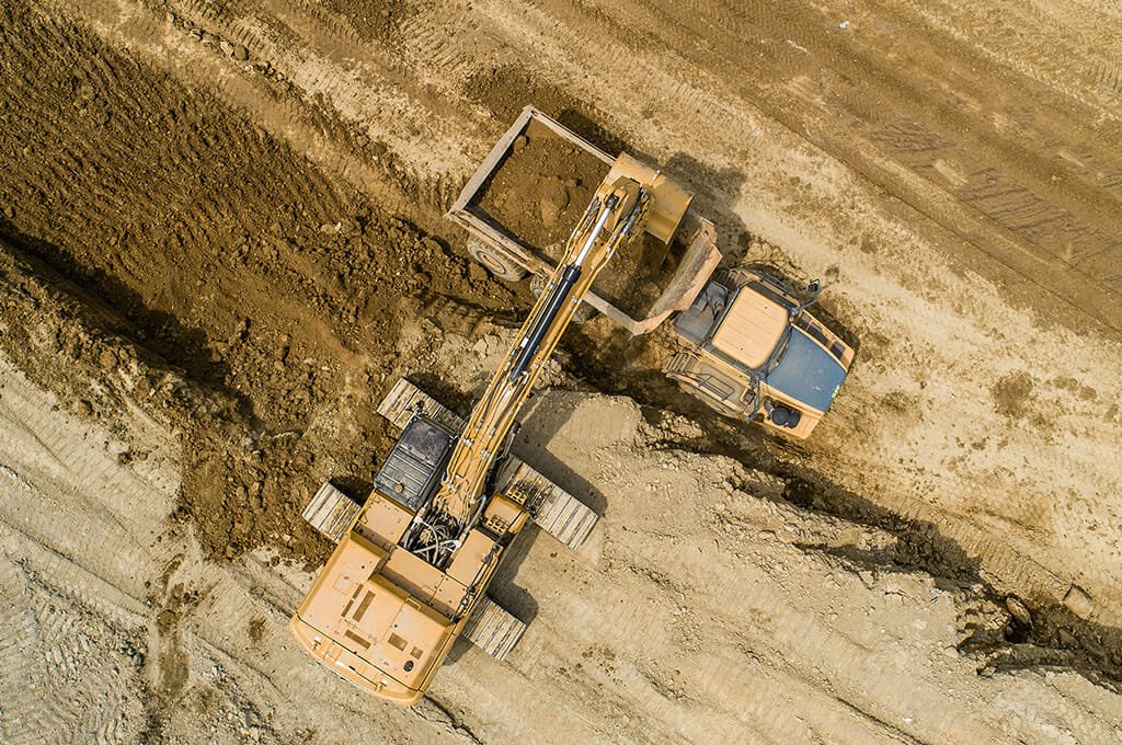 Aerial view straight overhead of excavator loading dirt into dump truck in dirt field