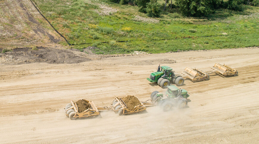 Aerial view of two green tractors with dirt work implements in dirt field