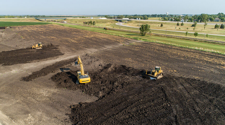 Aerial view of an excavator and two bulldozers clearing a dirt field
