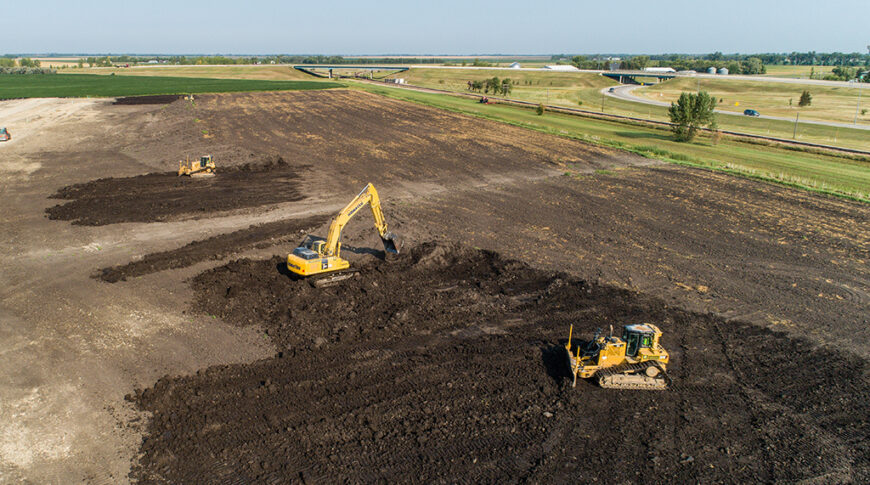 Aerial view of an excavator and two bulldozers clearing a dirt field