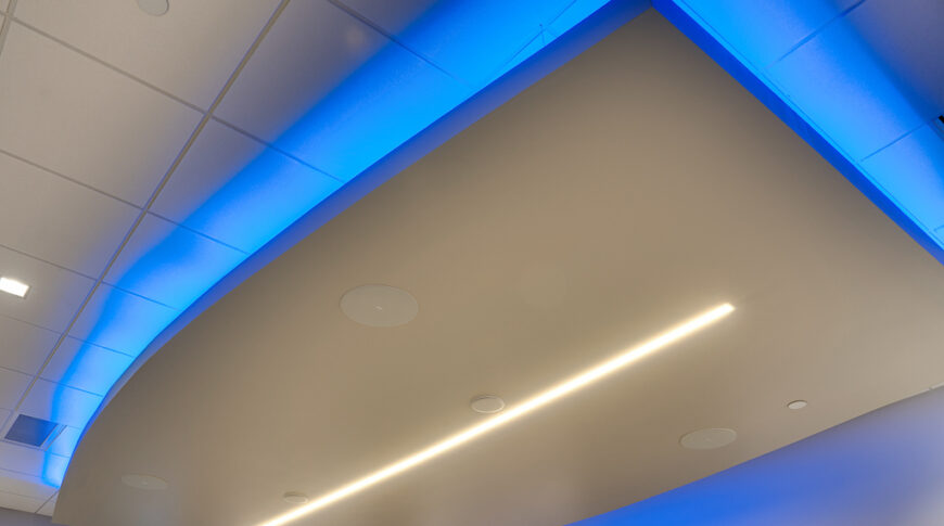Featured blue uplighting behind dropped rounded rectangular ceiling panel in large conference room.