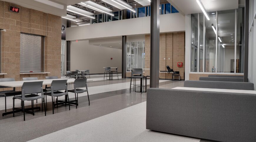 Back corner of high school commons area with long rectangular table and chairs and booths to the outside wall.