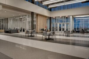 Entryway commons area of high school building with white, gray and dark gray striped floors, and small round tables and chairs throughout.