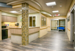 Hallway in hospital area with patient rooms to the right and back walls and a convenience station with mini fridge, microwave and sink to the left.