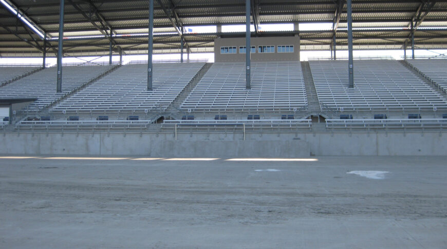 Track view of concrete ND State Fair Grandstands base with metal bleachers and steel beams upholding metal roof above.